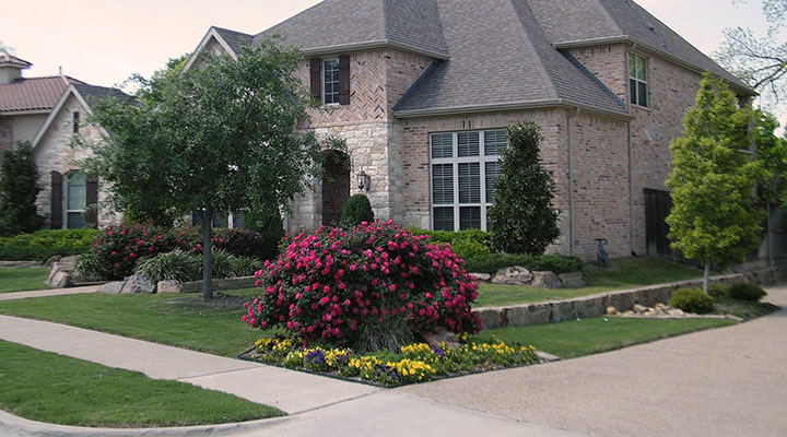 Beautifully landscaped yard featuring flowering bushes and
              mulched flower beds..